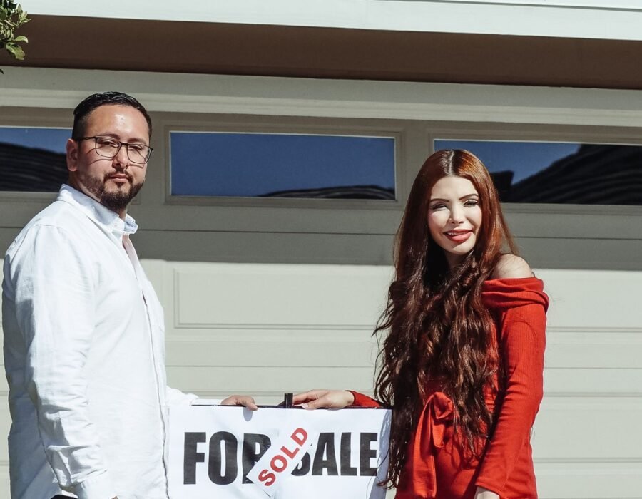 Happy couple standing outside their newly purchased home with a sold sign