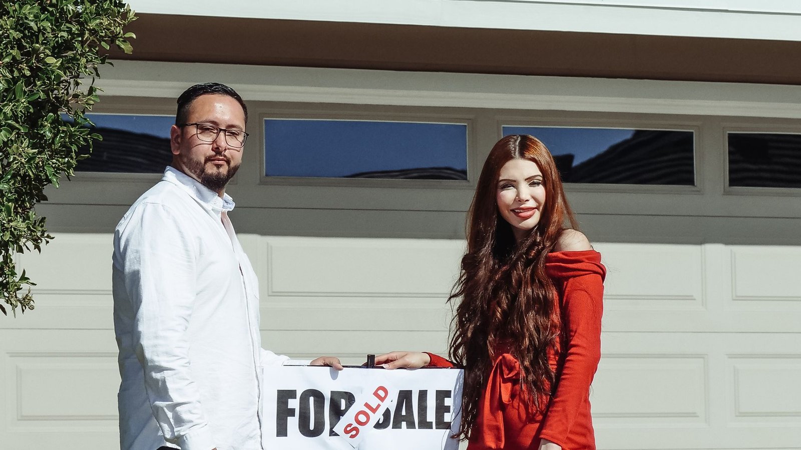 Happy couple standing outside their newly purchased home with a sold sign
