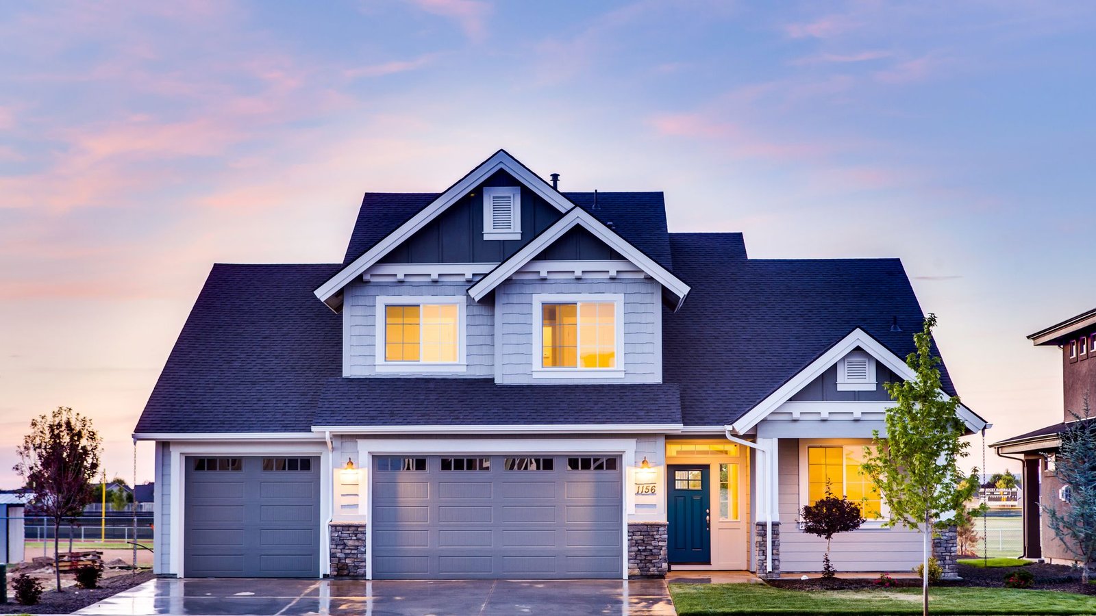 Two-story suburban house with warm lights in the windows at dusk